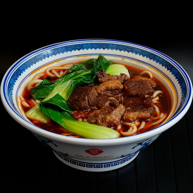 Bowl of noodle soup topped with braised beef and green vegetables in a blue-and-white bowl