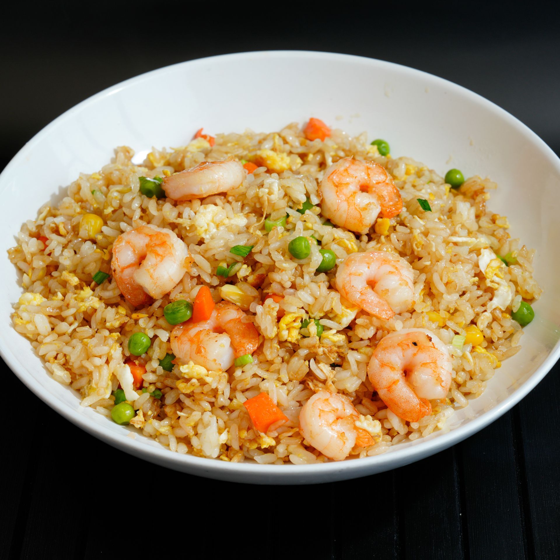 Bowl of shrimp fried rice with peas and carrots on a dark table