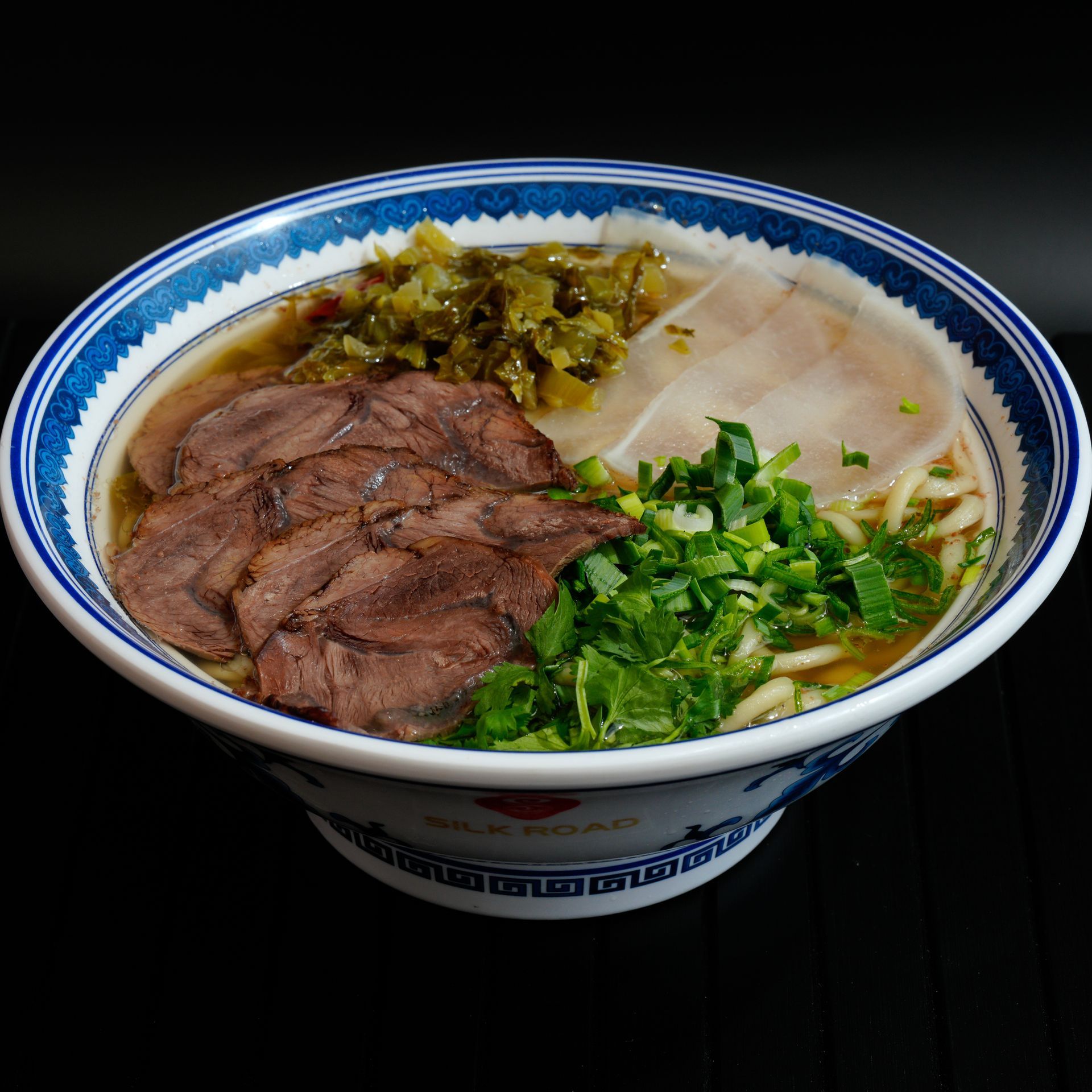 Bowl of noodle soup topped with sliced beef, green herbs, and pickled vegetables