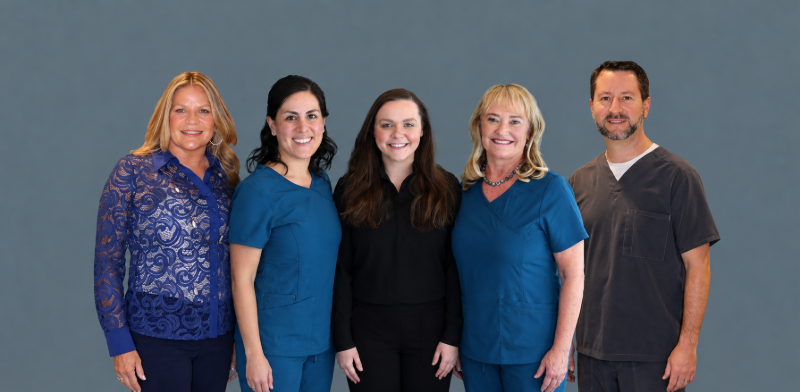 Five smiling coworkers posing shoulder to shoulder against a blue background