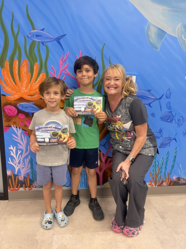 Three people holding certificates pose in front of a colorful underwater mural.