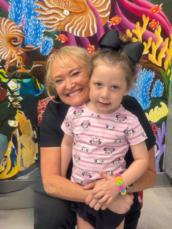Smiling woman hugging a child in front of a colorful mural