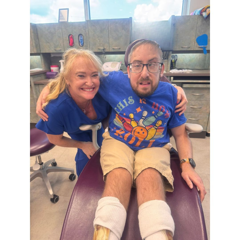 Two people smiling in a clinical room, seated close together on a padded exam chair.