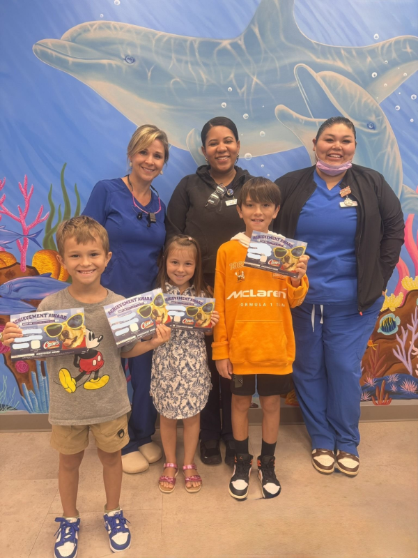 Group of six people posing indoors in front of a large shark mural, smiling and holding gift bags.