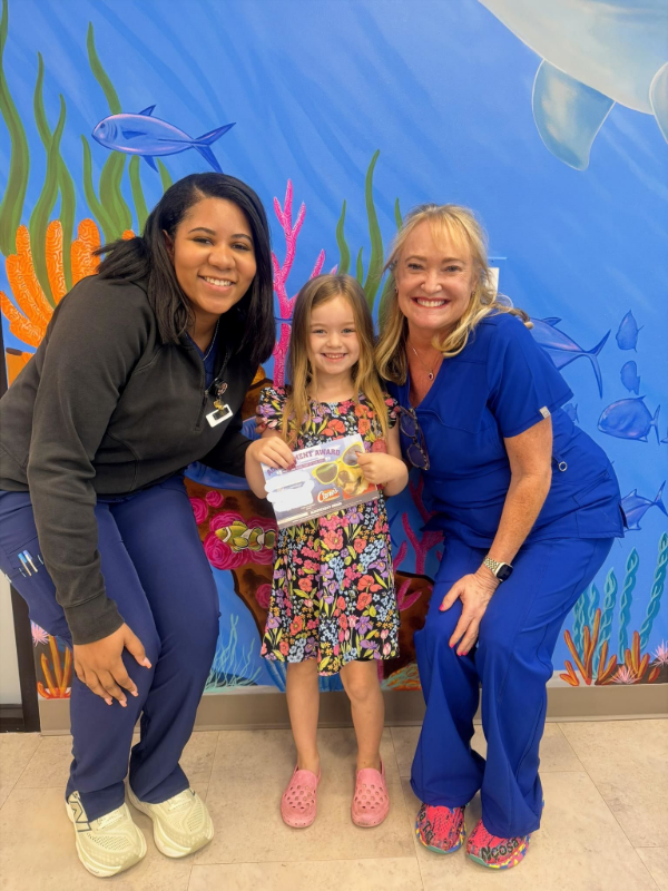 Three smiling people posing in front of a colorful ocean-themed mural, holding a certificate.