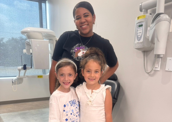 Three smiling children in a medical exam room, standing near dental equipment.