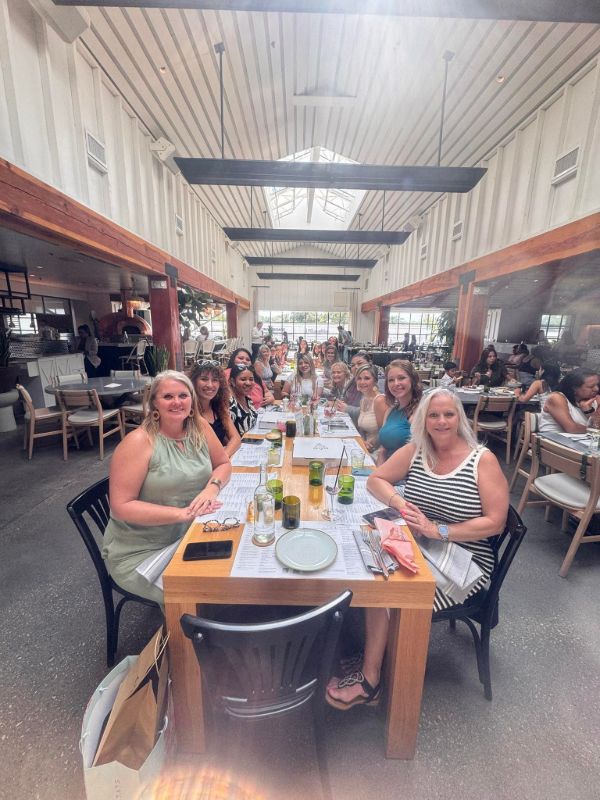 Long dining hall with people seated at a communal table, raising glasses and smiling