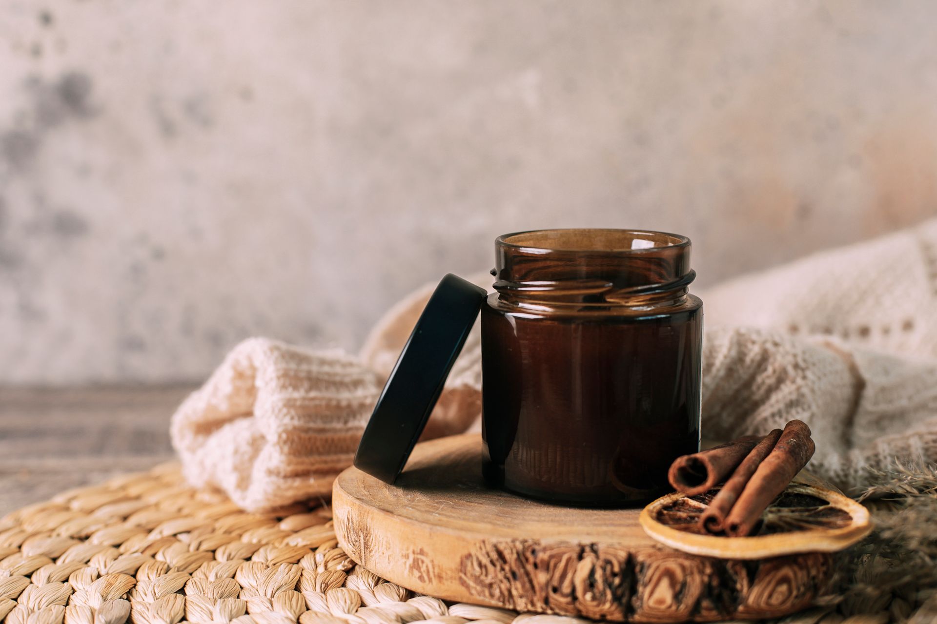 A jar of chocolate sauce with cinnamon sticks on a wooden tray.
