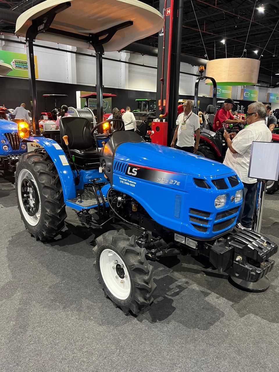 Trator LS azul com cortador de grama frontal em exposição em um estande interno.