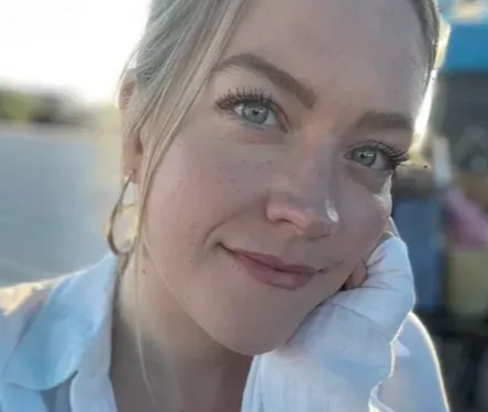 Close-up of a smiling woman resting her face on her hand outdoors in soft daylight