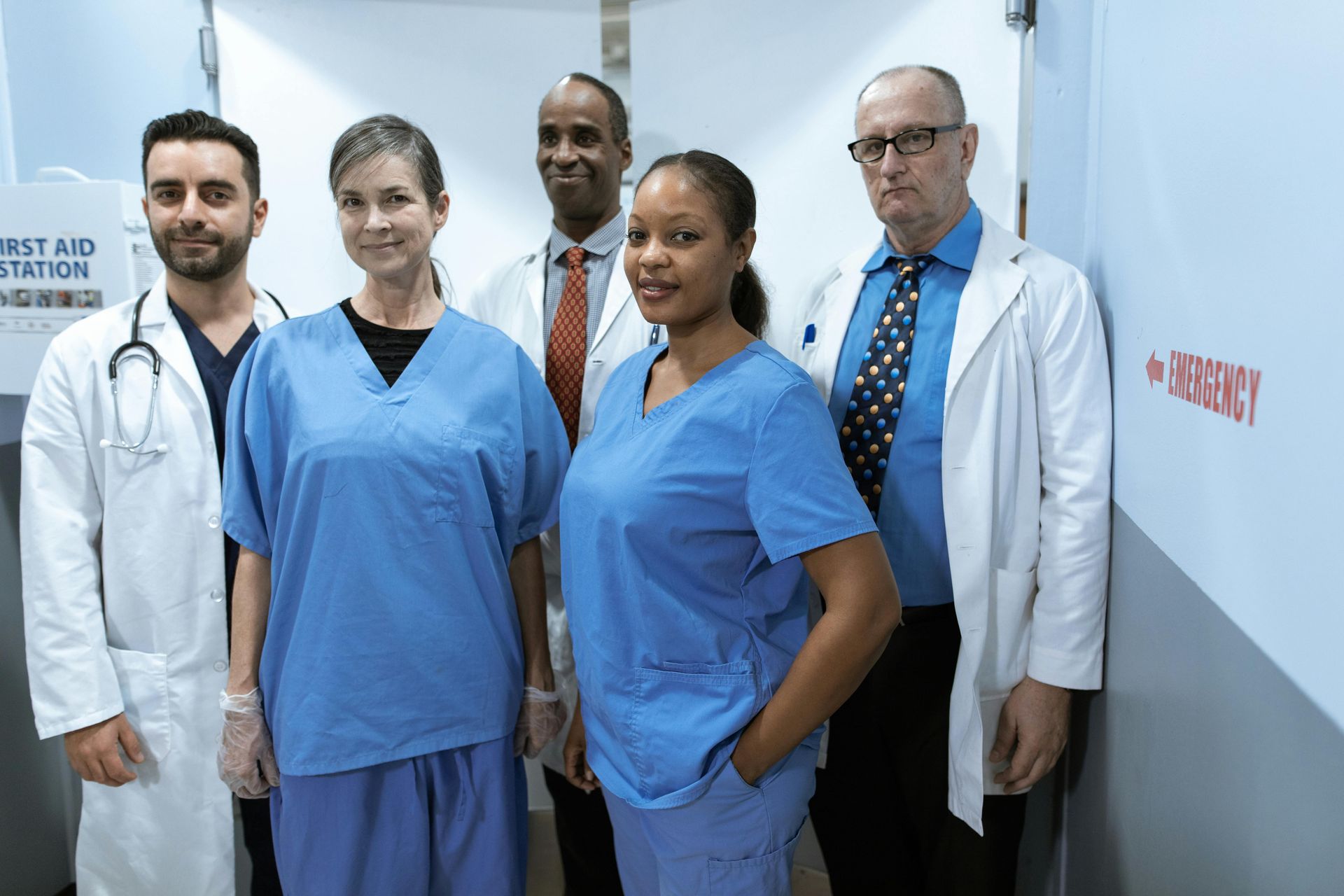 Medical staff in a hospital hallway. Team smiles at the camera, wearing scrubs and white coats.