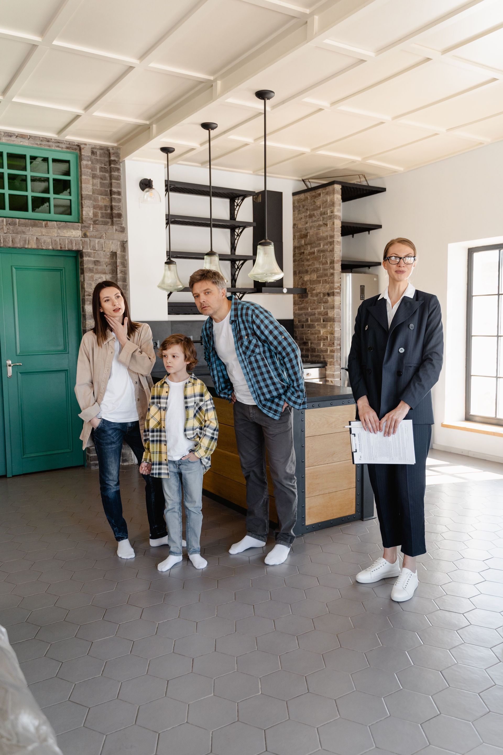 A family views a house with a realtor. Large windows with an outside view. The realtor gestures to the space.