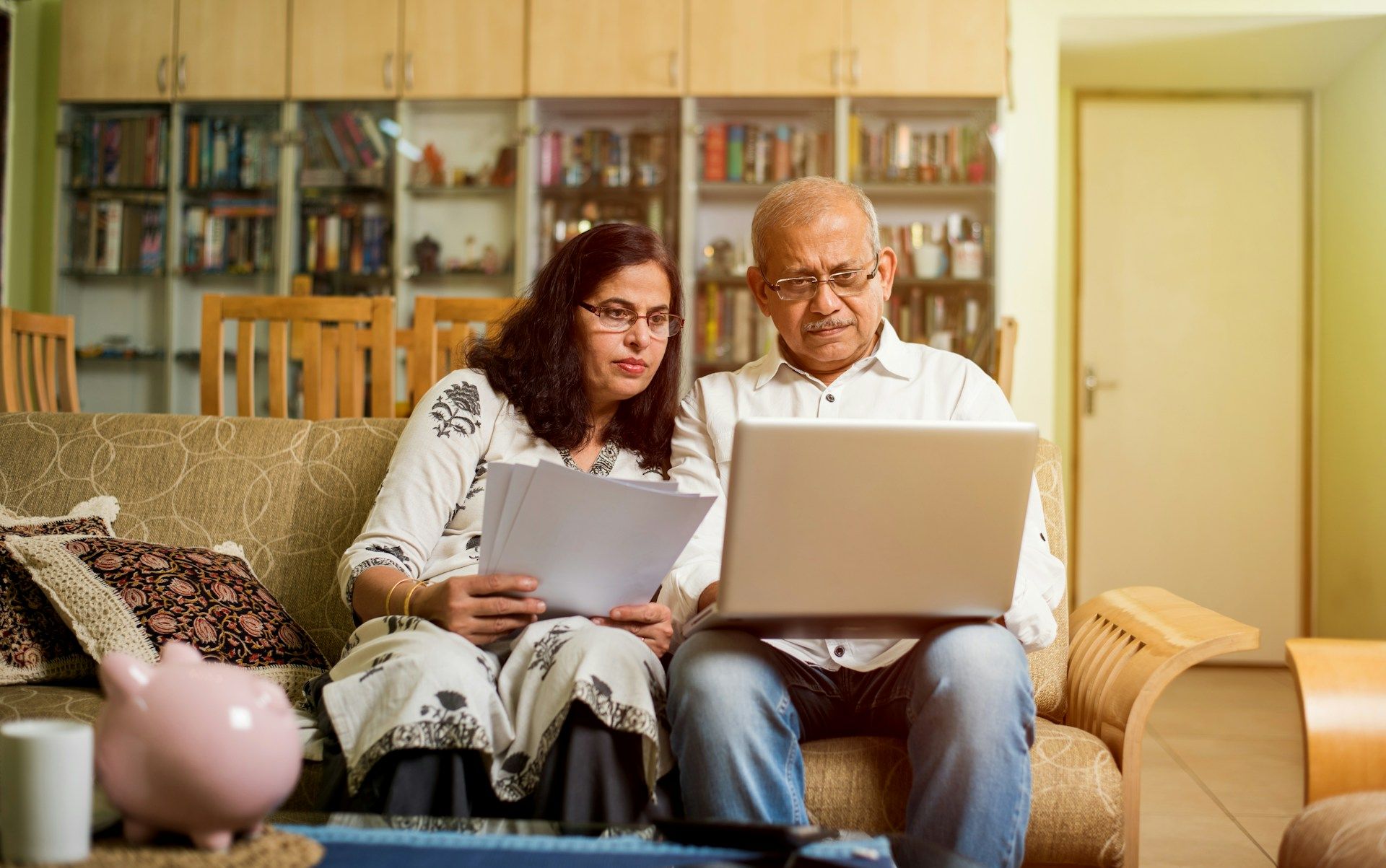 Two people on a couch using a laptop and reading papers in a cozy living room