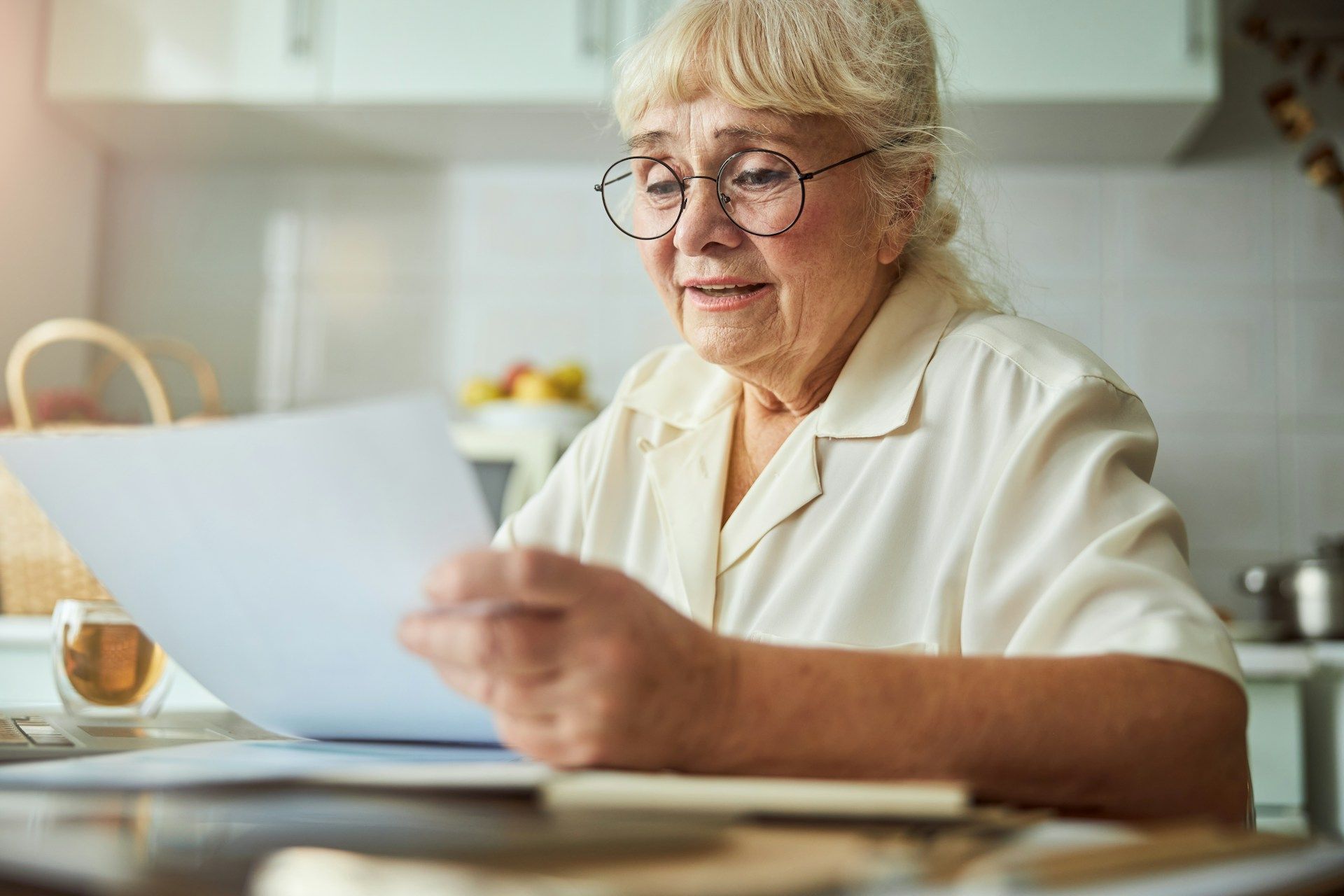 Person reading a document at a kitchen table, with a cup nearby and a bright home kitchen in the background