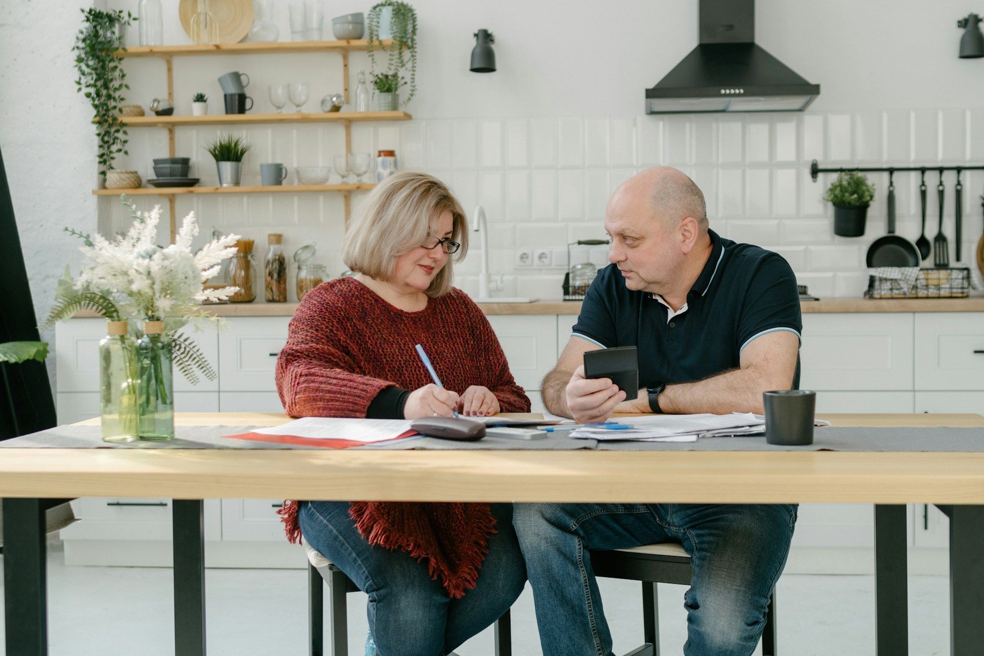 Two people talking over notes at a kitchen table in a bright, modern kitchen