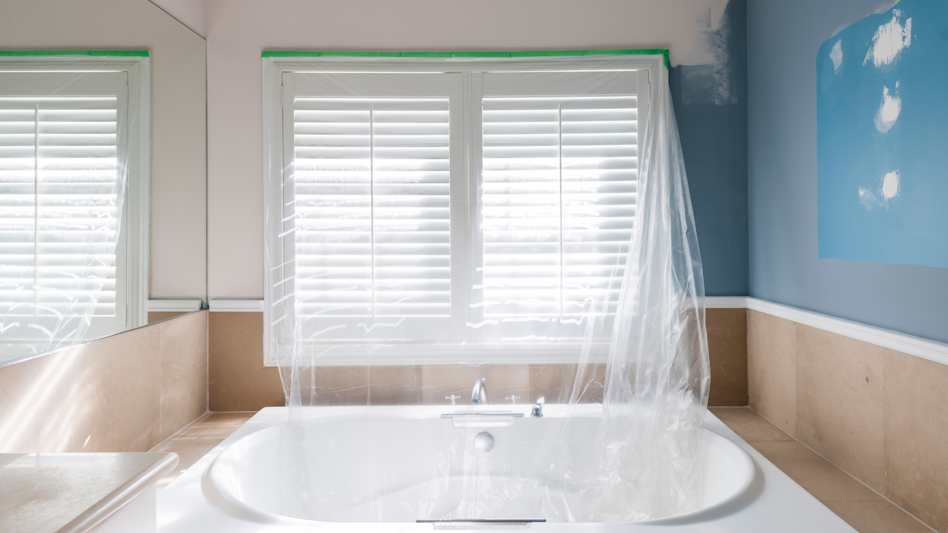 A bathroom with a bathtub and a window covered in plastic.