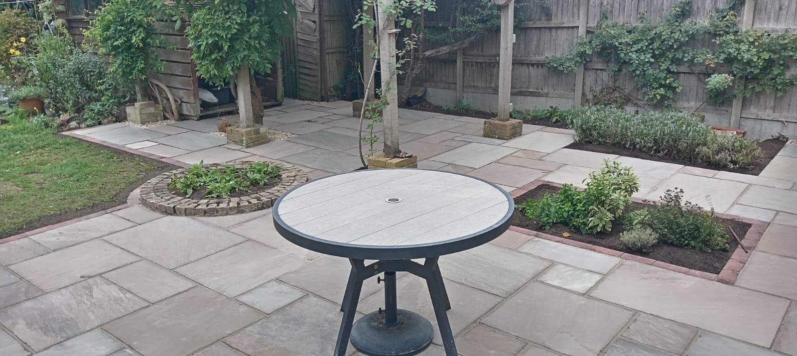 Round patio table in a landscaped backyard garden with stone pavers and shrubs