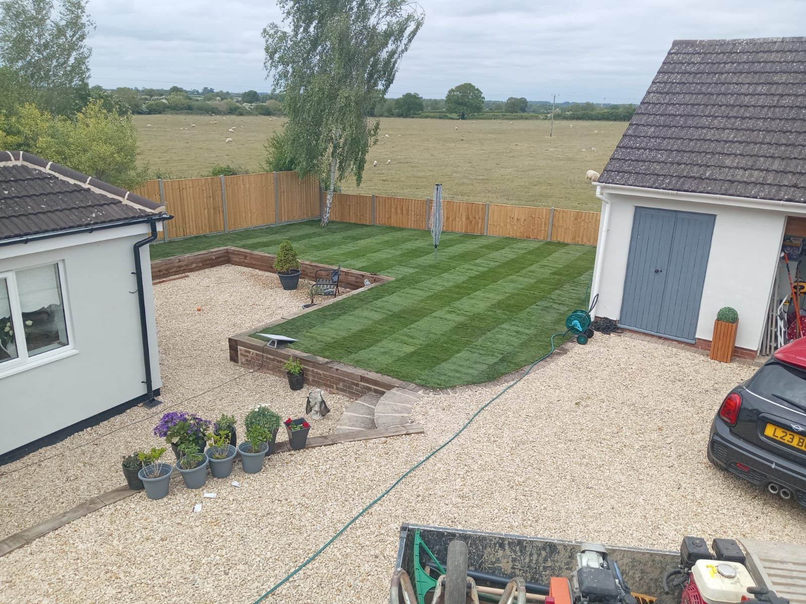 Backyard with gravel patio, striped lawn, raised flower bed, wooden fence, and two house walls.