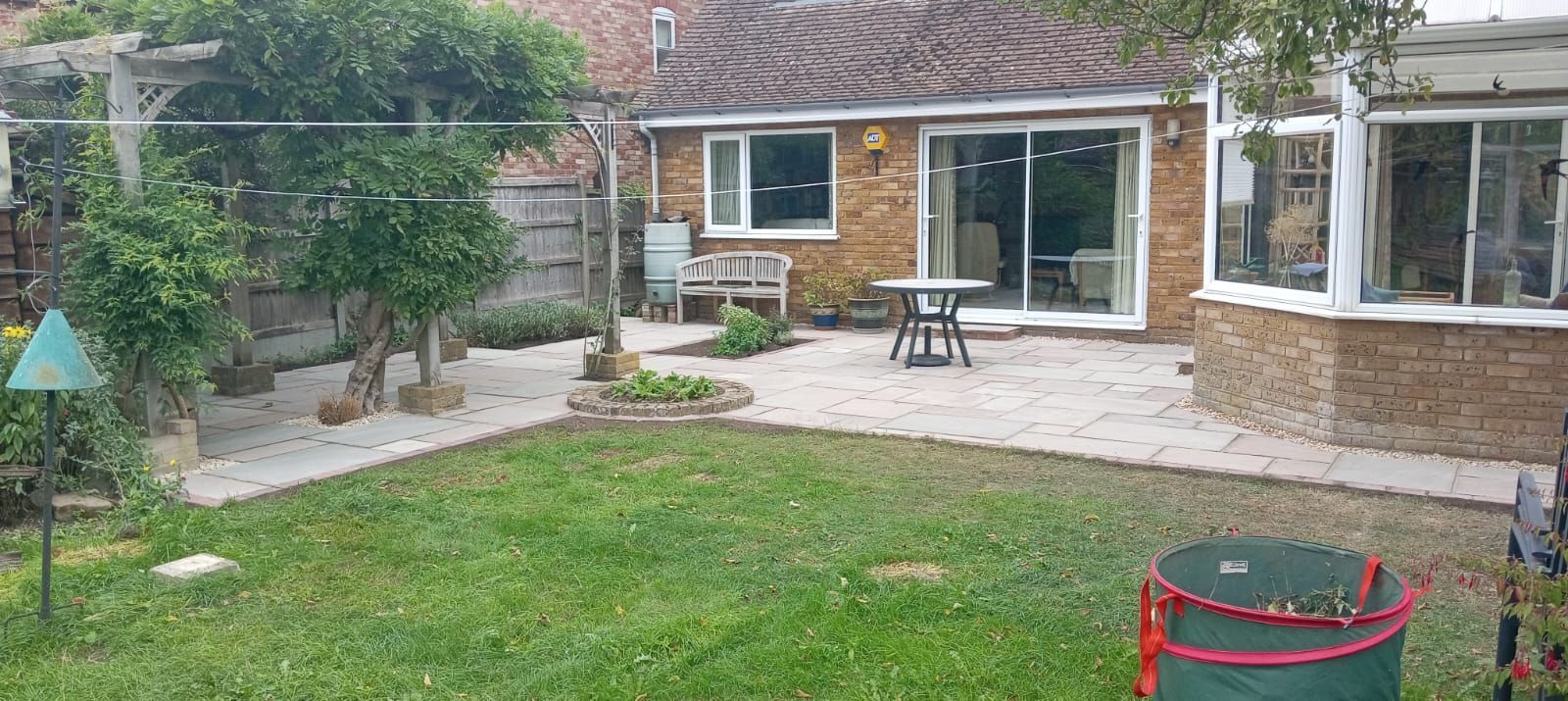 Backyard patio with lawn, stone seating area, small table, and house windows and sliding doors.