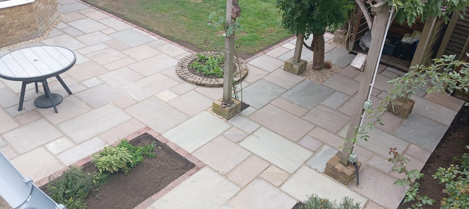 Courtyard with stone pavers, a round table, trees, and garden planters, viewed from above