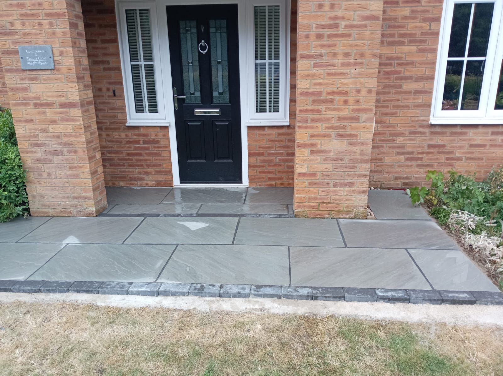 Front entrance with black door, brick walls, and a raised stone walkway leading to the porch.