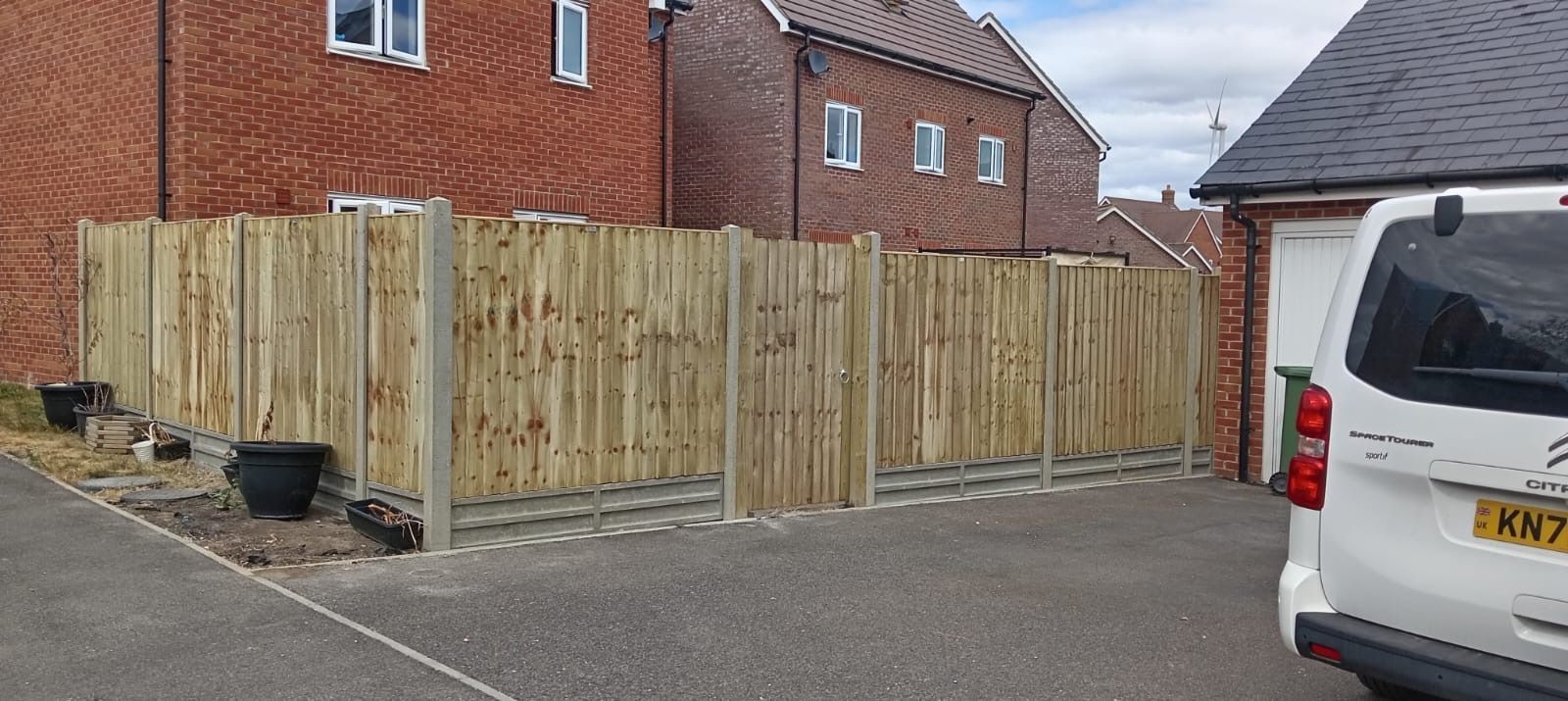 Wooden privacy fence beside a red brick house on a residential street, with a white van parked nearby.
