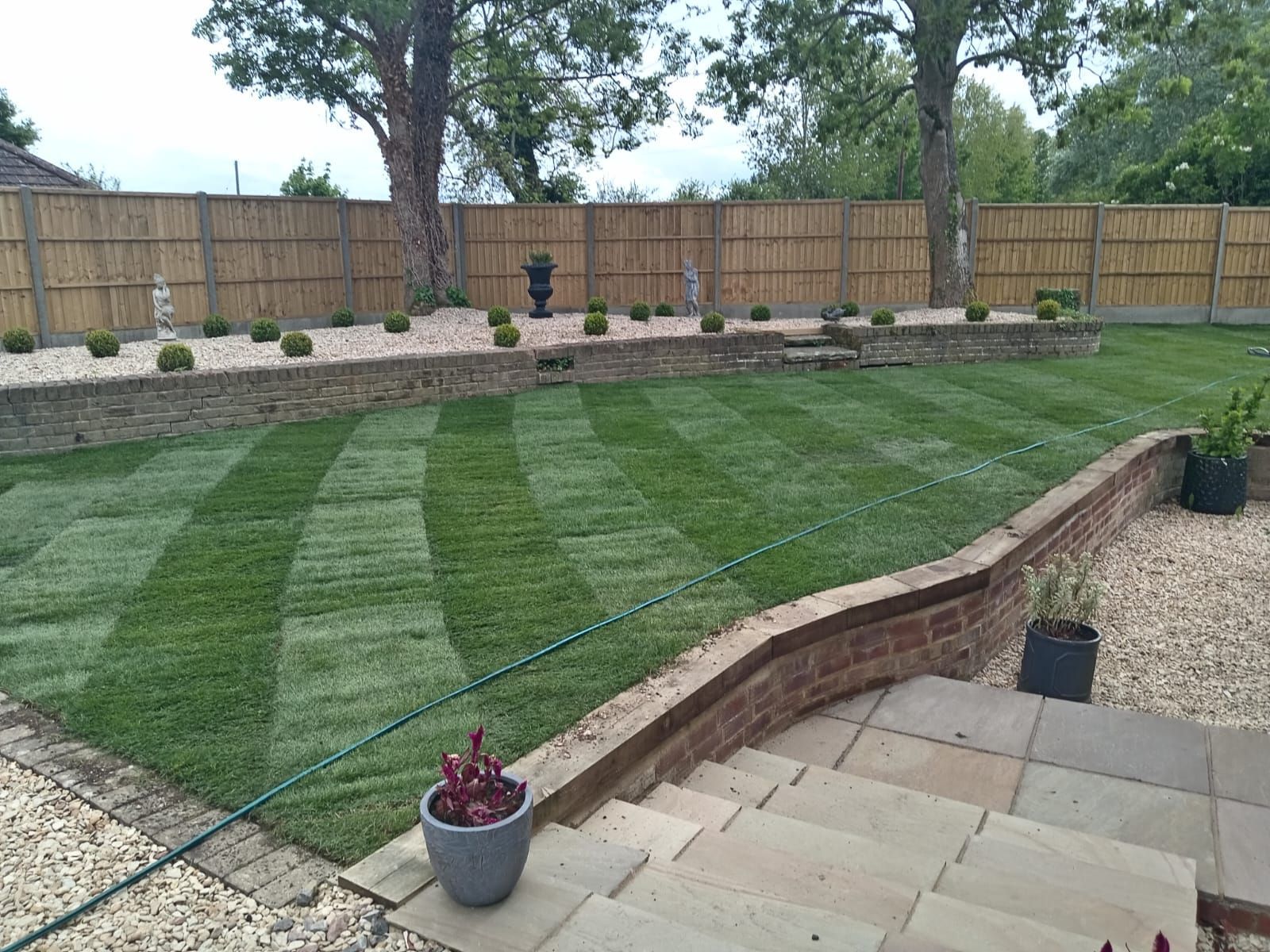 Backyard lawn with striped grass, stone steps, raised brick border, and wooden fence