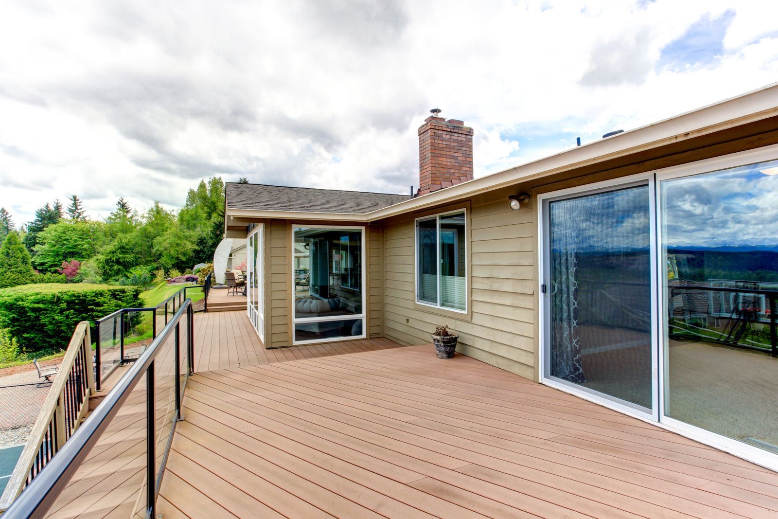 Brown deck with glass sliding doors, tan house, and brick chimney under cloudy sky.