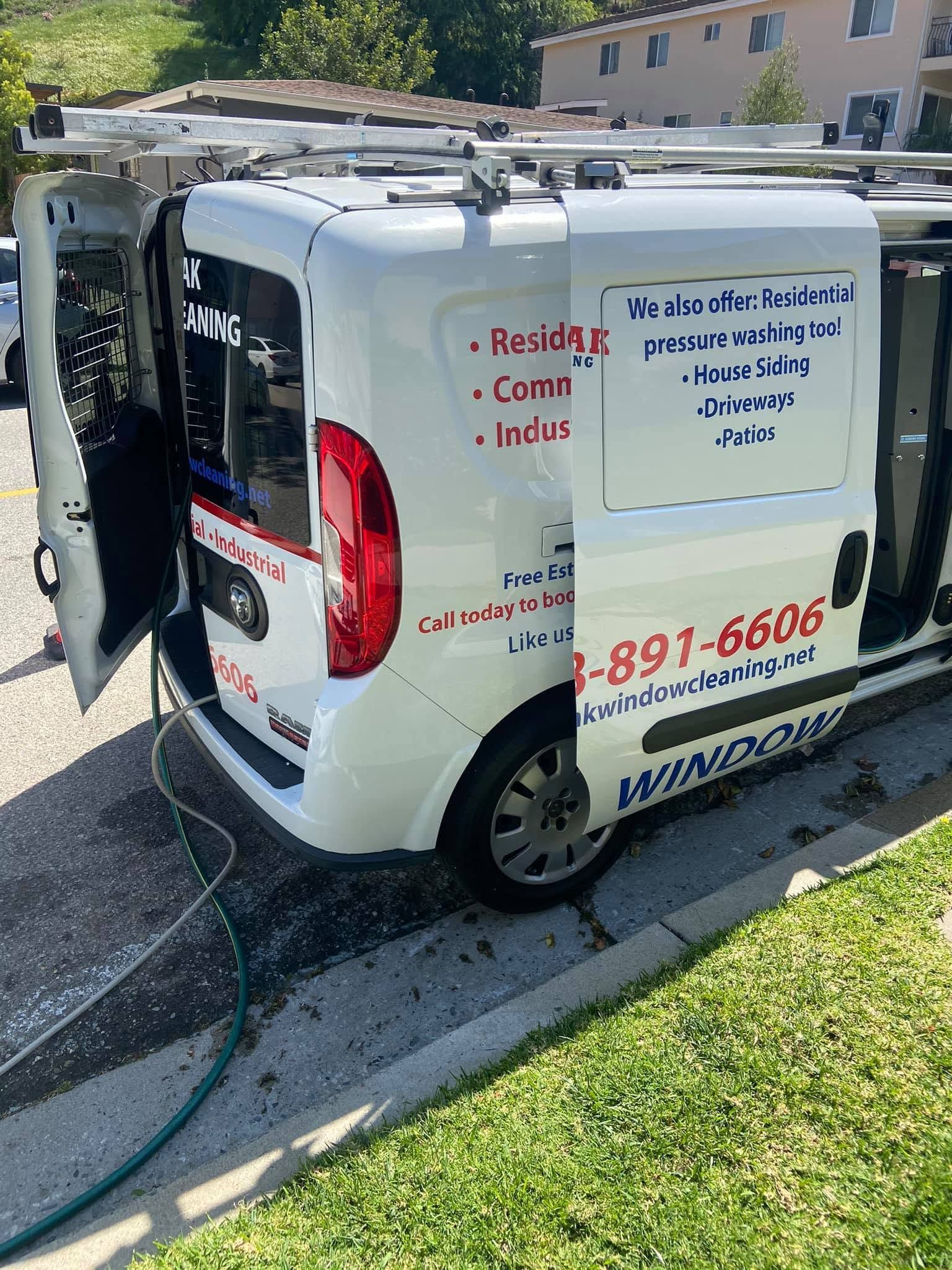White service van with ladder rack parked on a curb in a residential area, with company phone number and text on side.