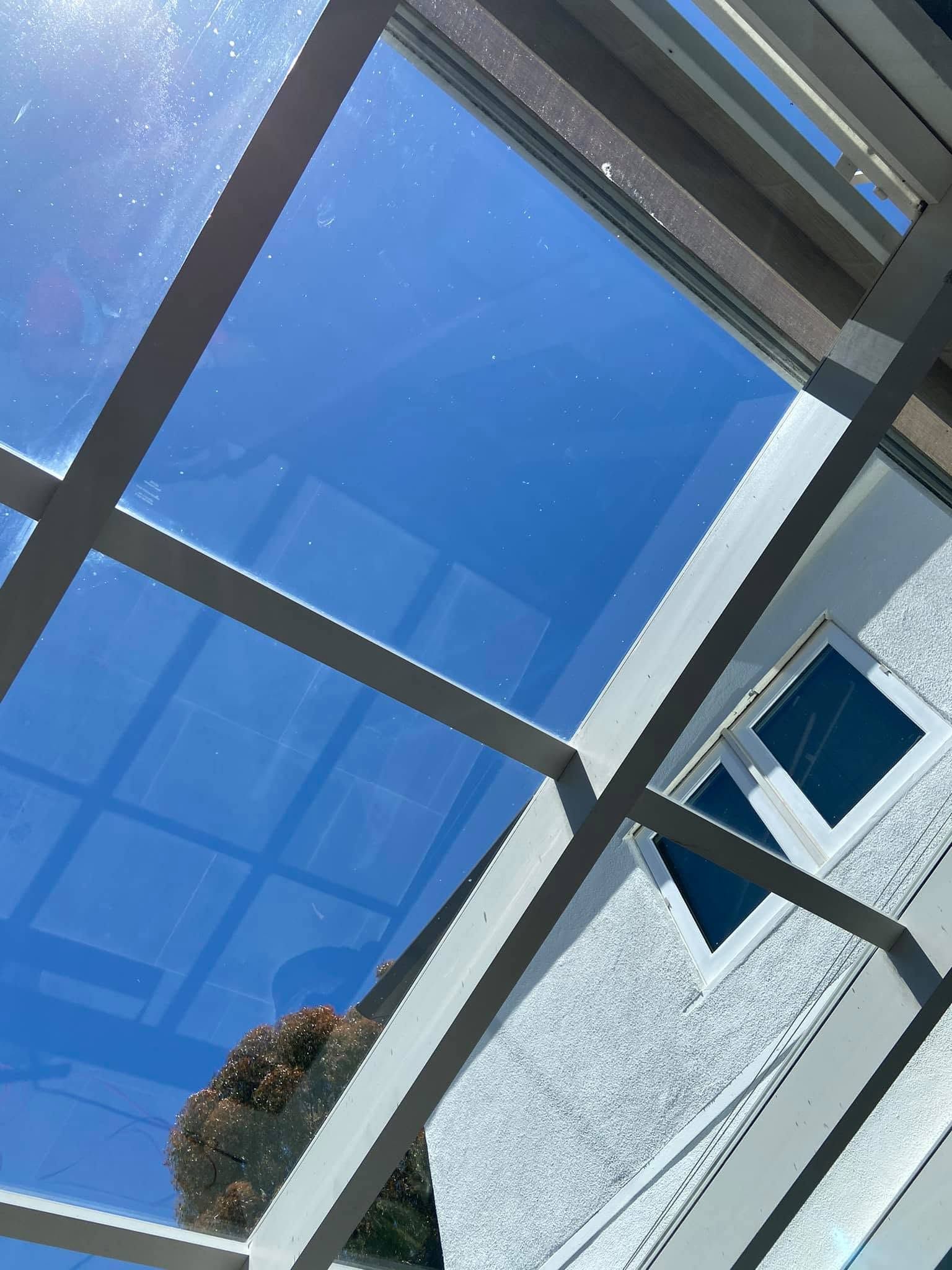 Blue sky seen through a tilted window frame beside a white building wall and small awning.