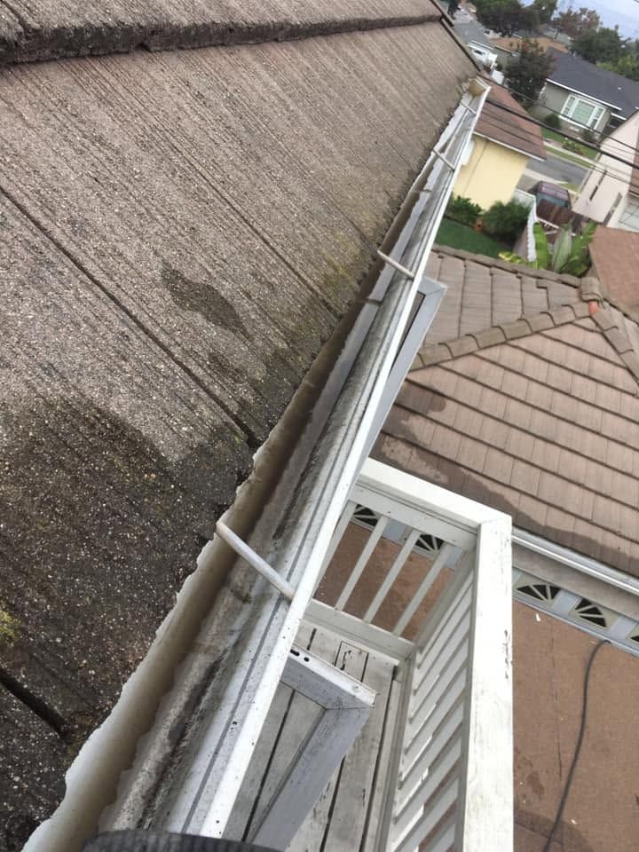 Steep rooftop view showing a gutter, neighboring roofs, and a residential street below
