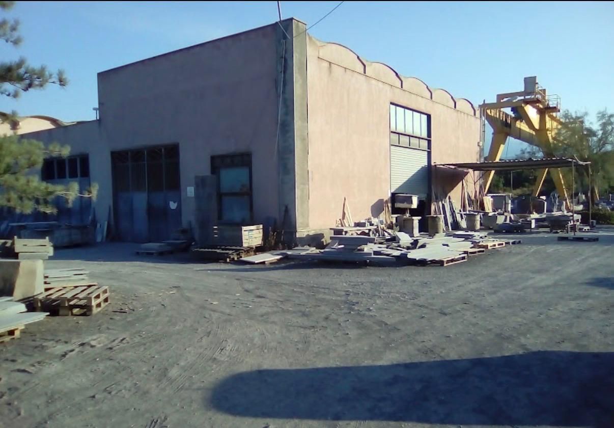 Edificio industriale in demolizione, con macerie e macchinari in un’area polverosa.