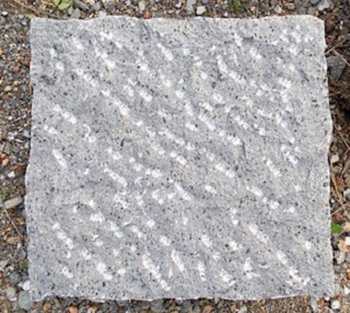 Piastrella quadrata in pietra grigia puntinata su un fondo di ghiaia