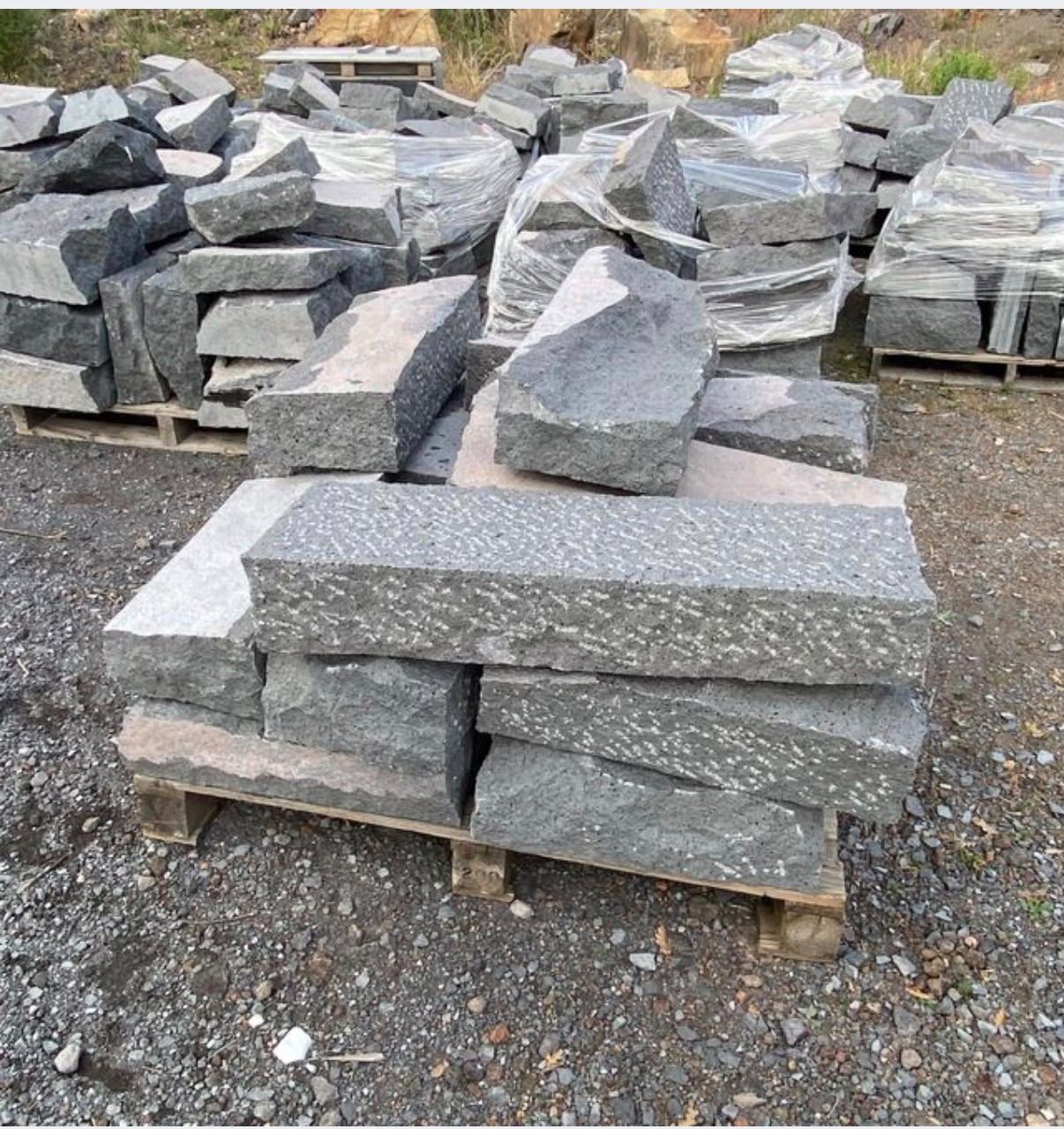 Pile di blocchi di pietra grigia tagliata su pallet di legno in un piazzale ghiaioso all’aperto