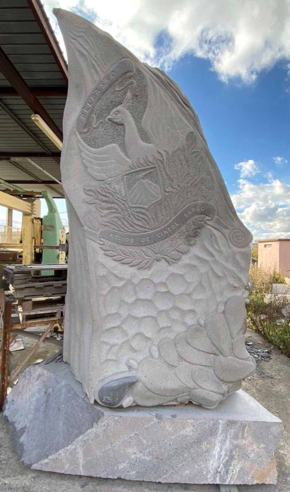 Alta scultura astratta in pietra con motivi a onde scolpiti, su un piedistallo all’aperto sotto una tettoia