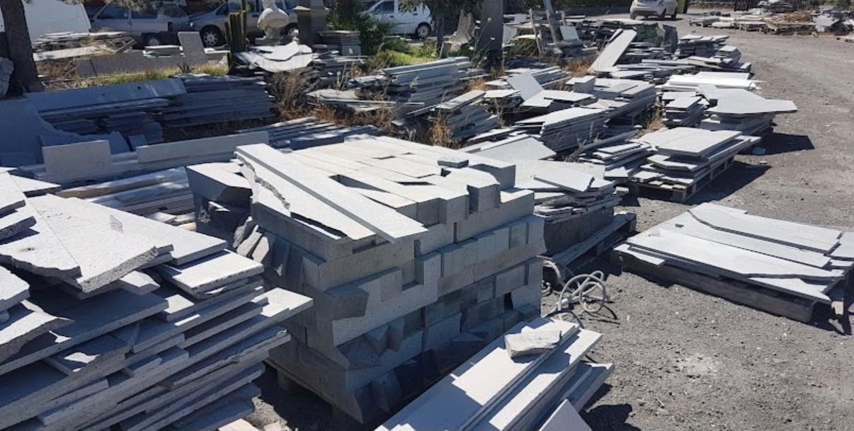Pile di materiali edili bianchi e lastre accatastati all’aperto in un piazzale ghiaioso.