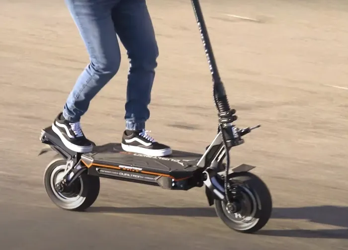 Person riding a black electric scooter on a paved surface. They wear jeans and Vans sneakers. -  EVA Motors in Paget, QLD