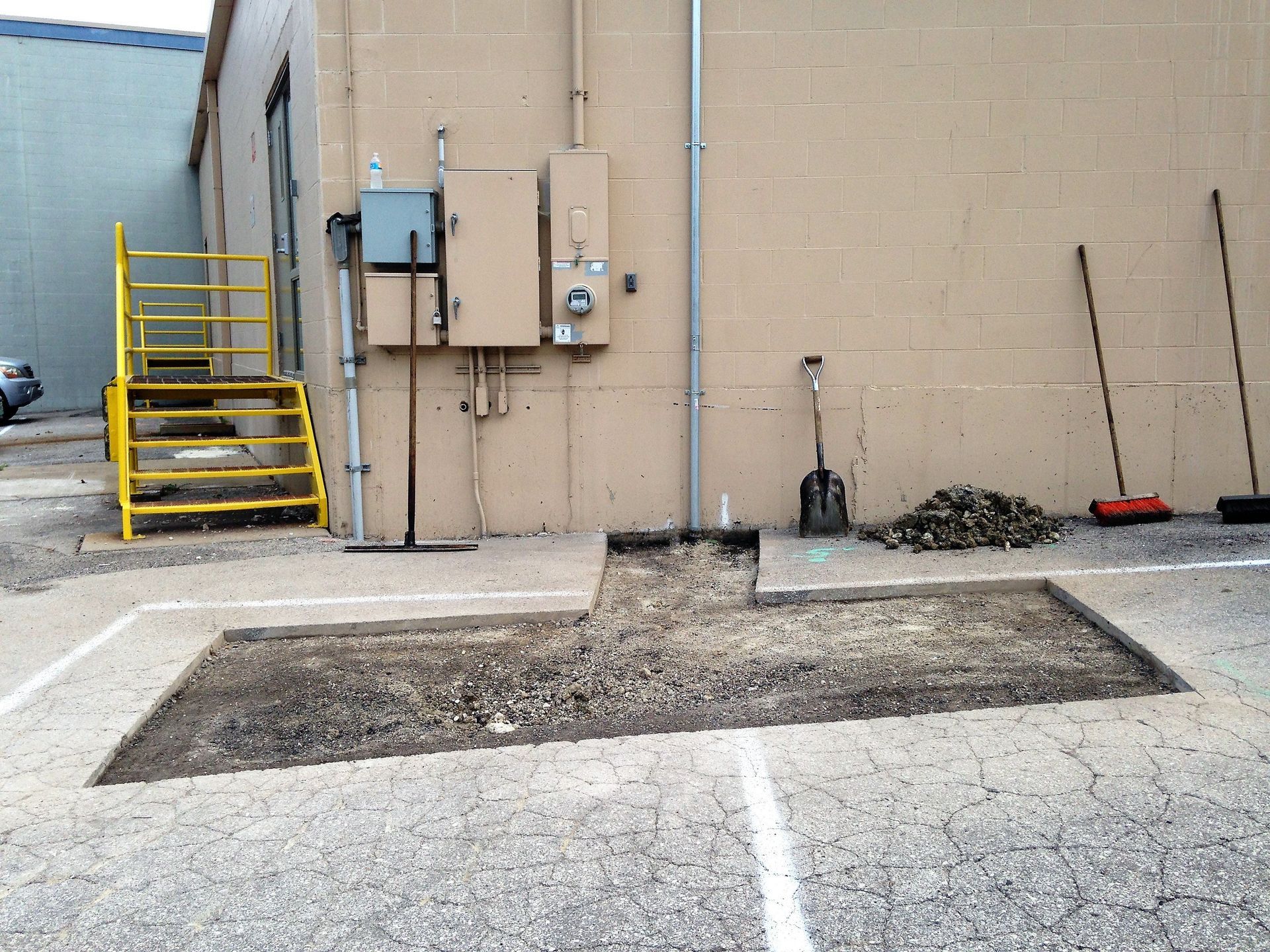 Industrial building wall with yellow stairs, utility boxes, and a concrete cutout in the pavement