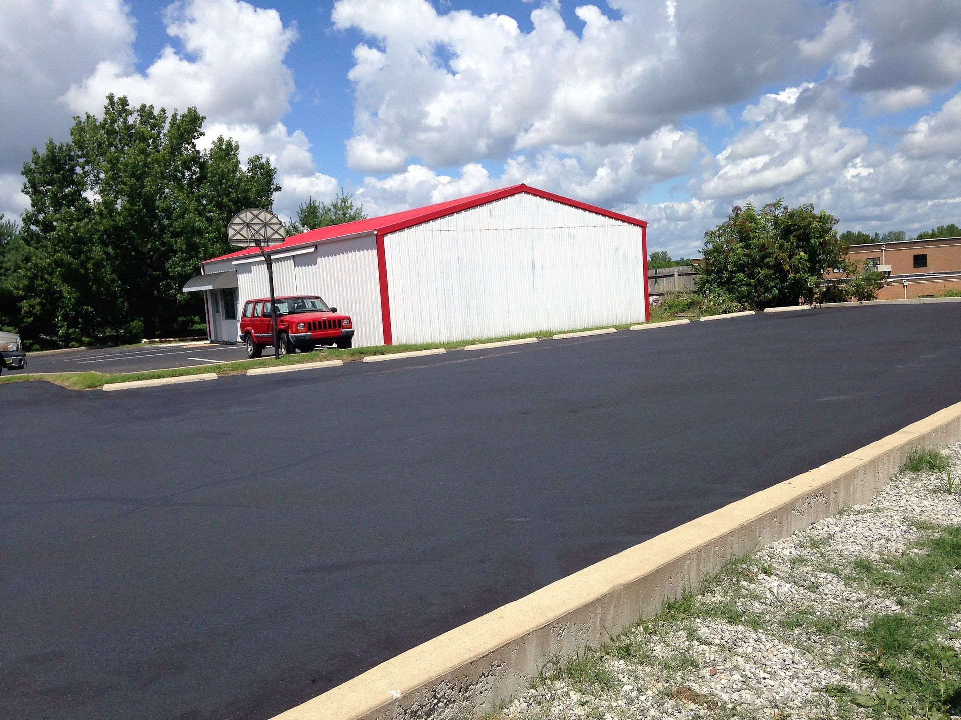 White building with red trim beside an empty blacktop lot under a cloudy sky