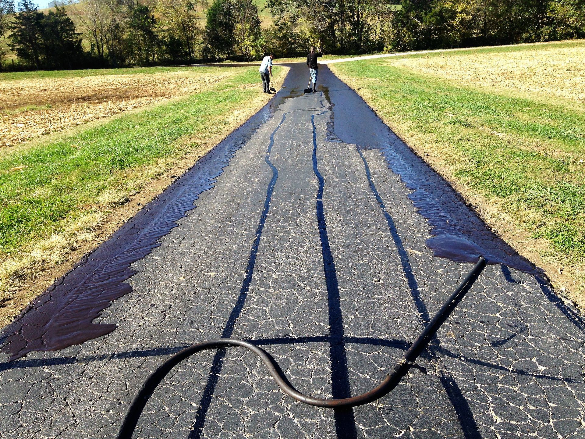 Cracked asphalt path with large patches and a hose crossing it in a grassy rural area