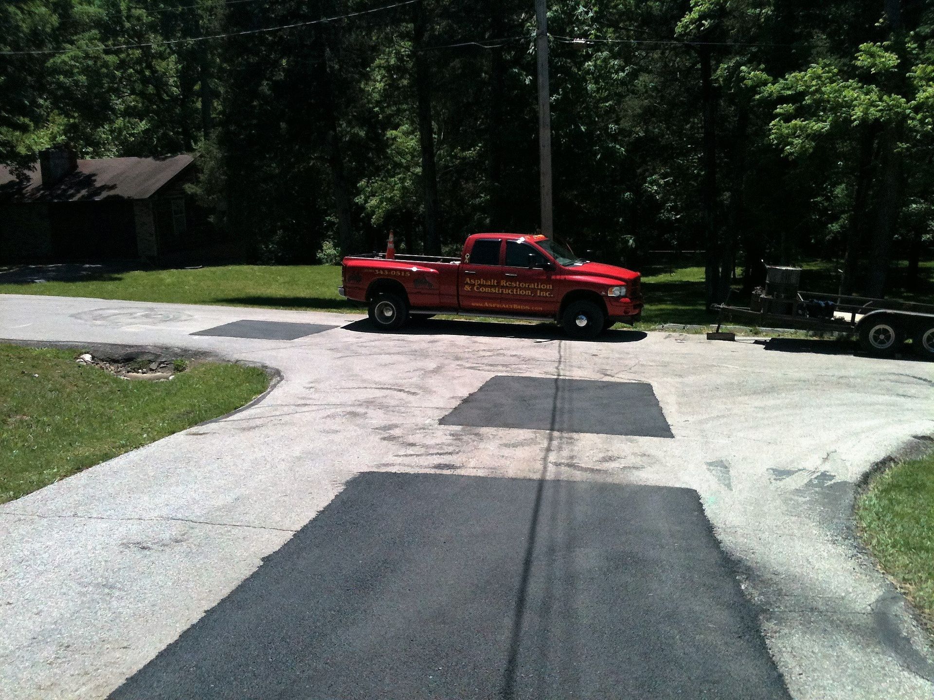 Red pickup truck on a driveway near trees and a trailer in a wooded area.