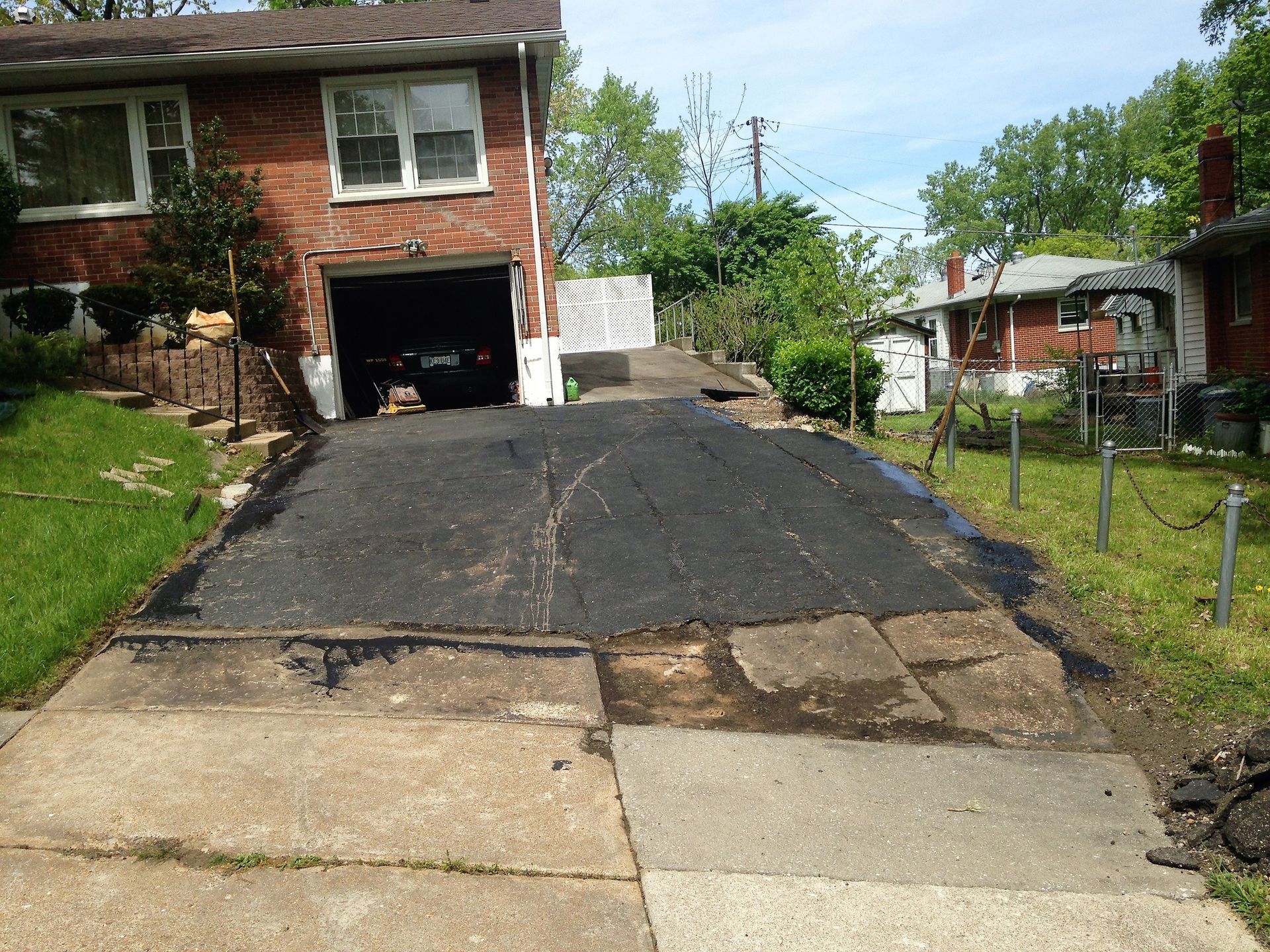 Steep cracked asphalt driveway leading to a brick house with an open garage and grassy yard