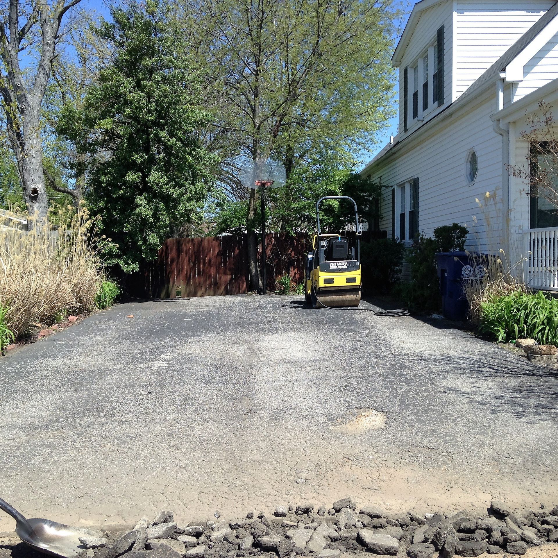 Gravel driveway beside a white house, with a small yellow loader near a wooden fence.