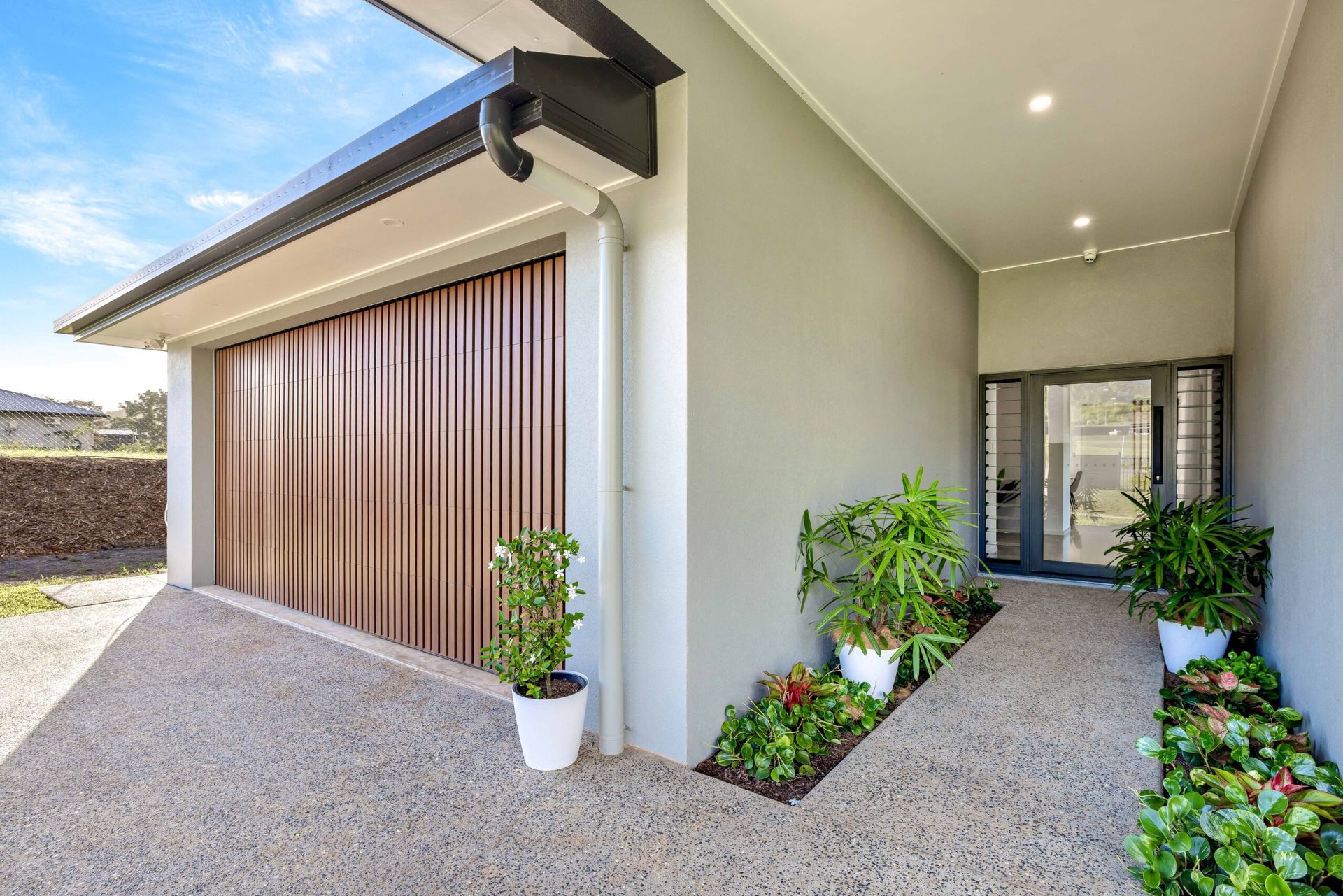 A white garage door is next to a brick building— Hastings Garage Door Services in Port Macquarie