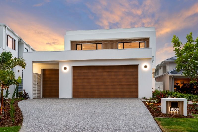 A Large Brick House With Two White Garage Doors and a Driveway — Hastings Garage Door Services in Port Macquarie