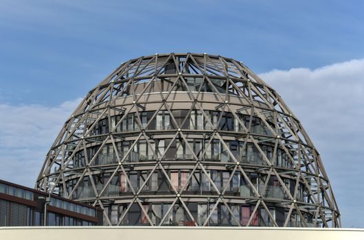 Cúpula de cristal moderna con una celosía de acero contra un cielo azul.