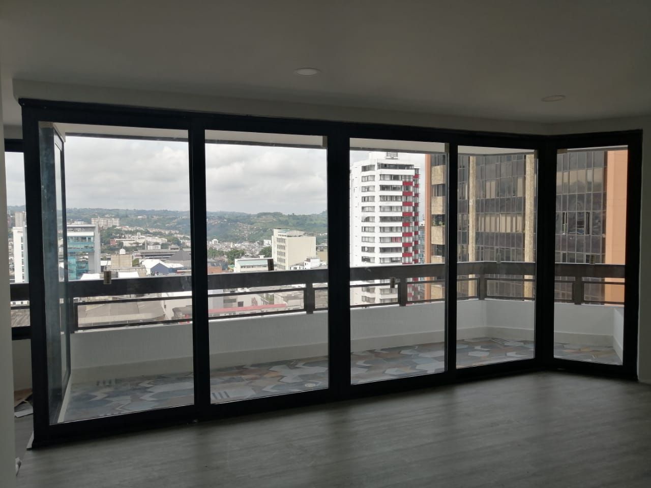 Vista en primer plano de la fachada acristalada de un edificio con una cuadrícula de vigas de acero gris que reflejan un cielo nublado.