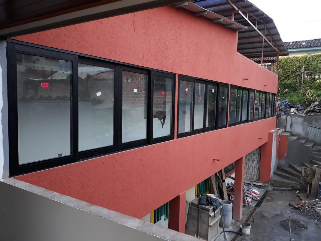 Una ventana con marco gris en una habitación blanca está ligeramente abierta por la parte superior, dejando ver el exterior.