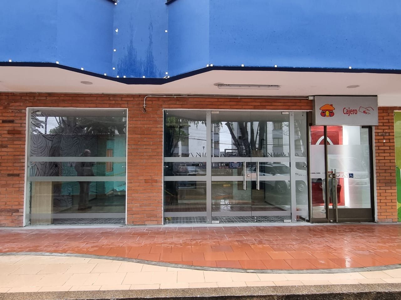 Un edificio moderno de cuatro plantas con una fachada de muro cortina de vidrio enmarcada por paneles metálicos grises, bajo un cielo despejado y luminoso.