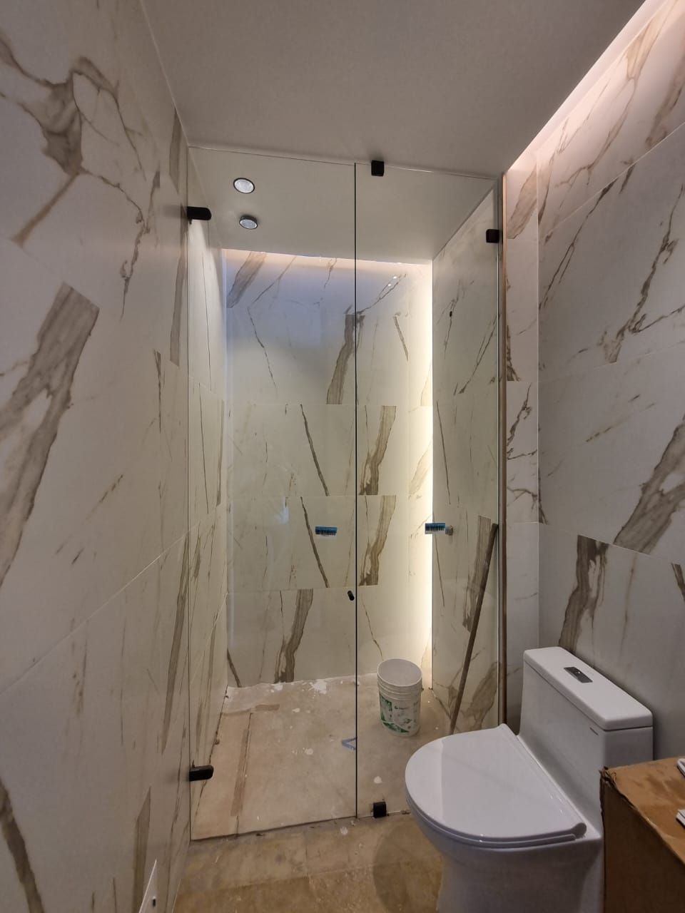 Un balcón moderno con barandilla de acero inoxidable y paneles de vidrio transparente con vistas a una terraza de madera y una puerta corredera de cristal.